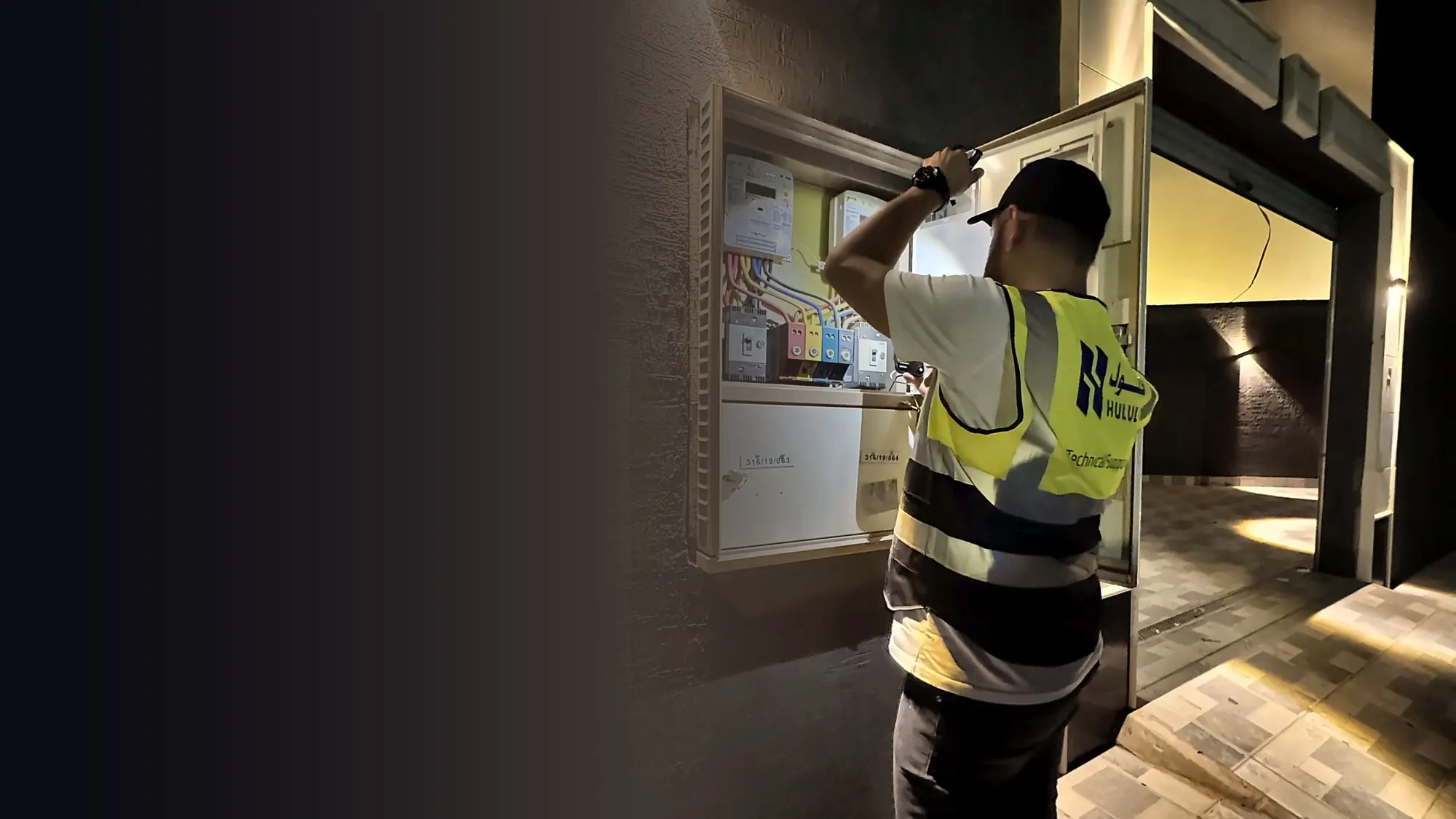 A Hulul technician in a branded vest inspecting an electricity meter panel